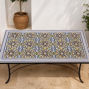 Peut inclure: Une table rectangulaire dotée d'un plateau en mosaïque avec un motif géométrique en étoile répétitif dans des tons de bleu, vert, jaune et blanc. La table possède un cadre en métal noir avec quatre pieds incurvés et une bordure décorative.