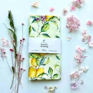 Puede incluir: Una bolsa de pan reutilizable de cera de abeja con un diseño de limón y flores. La bolsa mide 33 x 46 cm y presenta una banda blanca con el texto "Elle Makes Beeswax Bread Bag". La bolsa es ecológica y biodegradable.