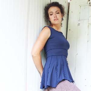May include: A woman wearing a navy blue sleeveless dress with a ruffled hem and a brown floral skirt.