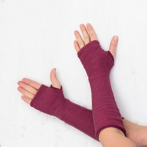 May include: A pair of burgundy fingerless arm warmers with thumb holes. The arm warmers are made of a soft, stretchy fabric.
