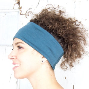 May include: A woman with curly brown hair is wearing a teal blue headband. She is wearing a maroon shirt.