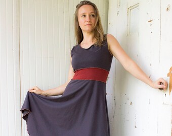 May include: A woman wearing a gray sleeveless dress with a red band at the waist. The dress has a scalloped hem and the woman is wearing brown sandals.
