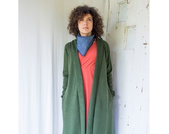 May include: A woman wearing a long, dark green cardigan with a hood over a coral-colored dress. She is wearing a blue bandana around her neck.