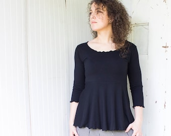 Puede incluir: Una mujer con una blusa negra de manga larga con volantes y una falda de rayas blancas y negras.