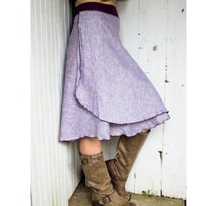 May include: A purple linen wrap skirt with a ruffled hem and a purple waistband. The skirt is being worn with brown leather boots.
