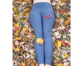May include: A person wearing blue leggings lying on a bed of autumn leaves. The leggings are a solid blue colour. A red and yellow leaf rests on the leggings. The leaves are in shades of yellow, orange, and brown.