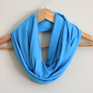 May include: A bright blue infinity scarf made of soft fabric, hanging on a wooden hanger.