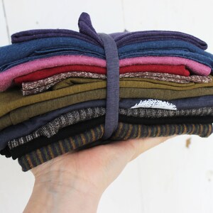 Puede incluir: Una pila de recortes de tela doblados en varios colores y patrones, incluyendo morado, azul, rosa, rojo, marr&oacute;n, verde, gris y negro. La tela est&aacute; agrupada con una banda el&aacute;stica.