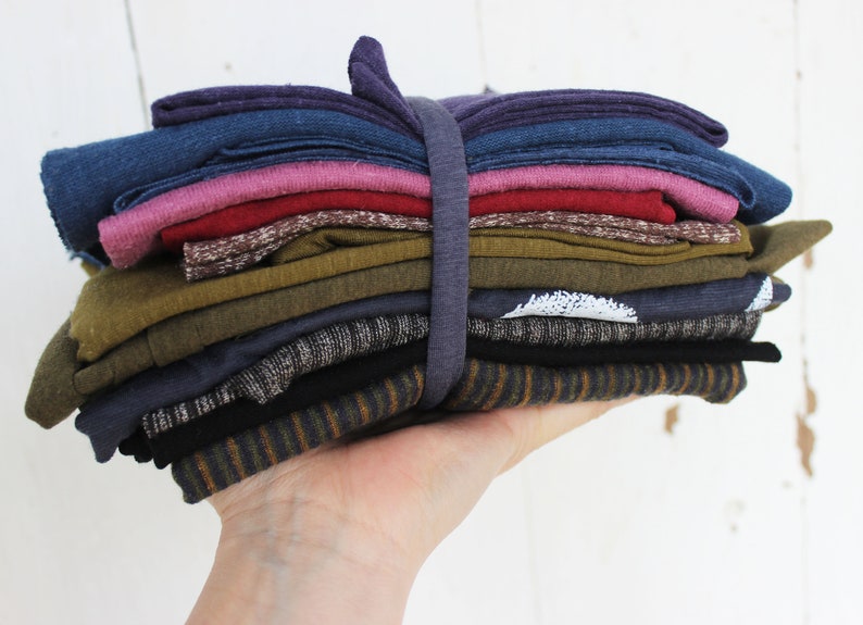 Puede incluir: Una pila de recortes de tela doblados en varios colores y patrones, incluyendo morado, azul, rosa, rojo, marr&oacute;n, verde, gris y negro. La tela est&aacute; agrupada con una banda el&aacute;stica.