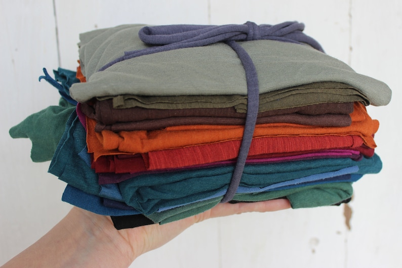 Puede incluir: Una pila de recortes de tela en varios tonos de verde, marr&oacute;n, naranja, rojo y azul, atados con un cord&oacute;n morado.