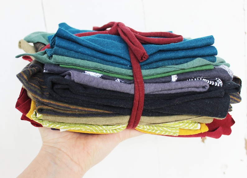 Puede incluir: Una pila de recortes de tela doblados en varios colores, incluyendo rojo, verde, azul, negro y amarillo, atados con una cinta roja.