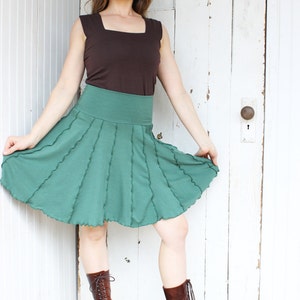 May include: A woman wearing a brown tank top and a green skirt with a ruffled hem. She is wearing brown lace-up boots.