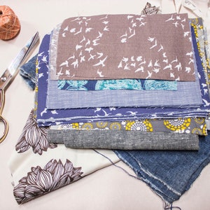Puede incluir: Una pila de recortes de tela en varios colores y patrones, incluyendo un estampado floral azul y blanco, una tela gris con p&aacute;jaros blancos y una tela a rayas azul y blanco. Los recortes de tela est&aacute;n dispuestos en una pila sobre una superficie blanca.