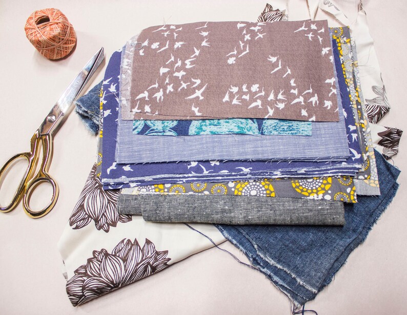 Puede incluir: Una pila de recortes de tela en varios colores y patrones, incluyendo un estampado floral azul y blanco, una tela gris con p&aacute;jaros blancos y una tela a rayas azul y blanco. Los recortes de tela est&aacute;n dispuestos en una pila sobre una superficie blanca.