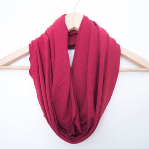 May include: A burgundy infinity scarf hanging on a wooden hanger against a white background.