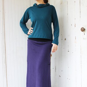 May include: A teal long-sleeved shirt with a cowl neck and a purple maxi skirt.