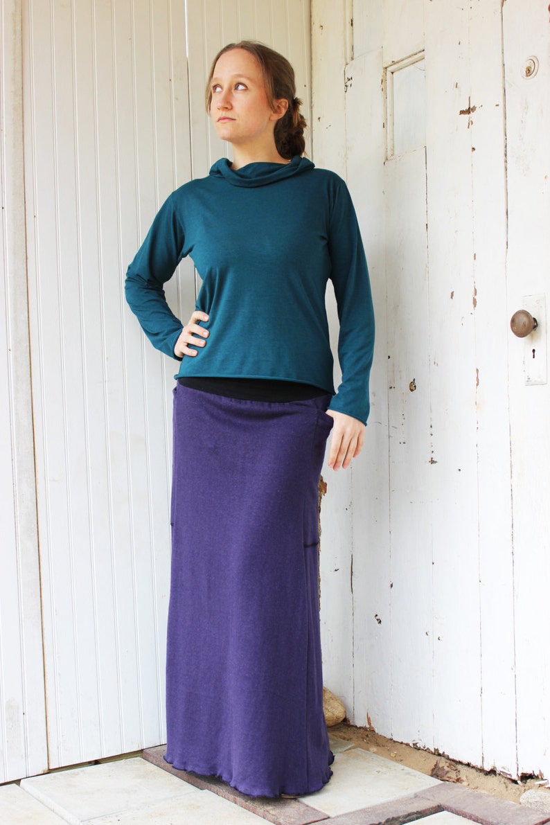 May include: A teal long-sleeved shirt with a cowl neck and a purple maxi skirt.