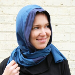 May include: A blue and dark blue hooded scarf made of soft fabric. The scarf is worn by a person with blonde hair.