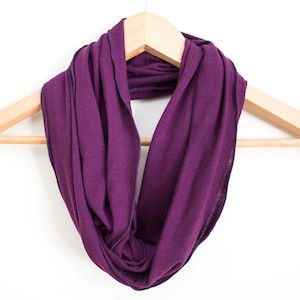 May include: A purple infinity scarf hanging on a wooden hanger. The scarf is made of a soft, stretchy fabric and has a simple, elegant design.