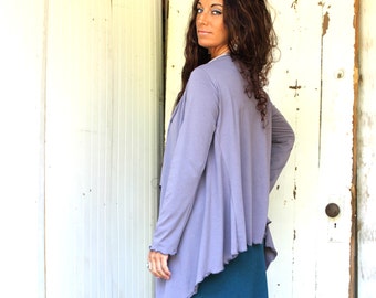 May include: A woman wearing a long-sleeved, light purple cardigan with a draped, asymmetrical hem. The cardigan is made of a soft, flowing fabric. She is wearing a teal blue skirt.