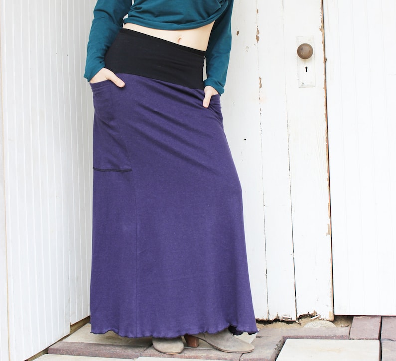 May include: A long purple skirt with a black waistband and a pocket on the left side.
