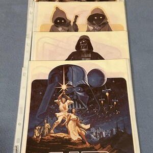 May include: A set of five Star Wars posters featuring various characters and scenes from the original movie. The posters are printed on white paper and have a vintage look.