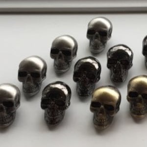 May include: A collection of 15 silver, black and gold skull-shaped buttons. The buttons are small and have a detailed skull design.
