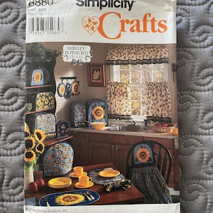 May include: A Simplicity Crafts pattern packet featuring a sunflower design. The packet includes a variety of kitchen items, such as curtains, placemats, and a tea cozy. The packet is labeled "8880" and "ONE SIZE".