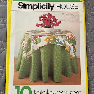 May include: A Simplicity House pattern package for 10 table covers. The package has a yellow border and features an image of a table with a green and white floral tablecloth. The text "Simplicity House" is displayed prominently.