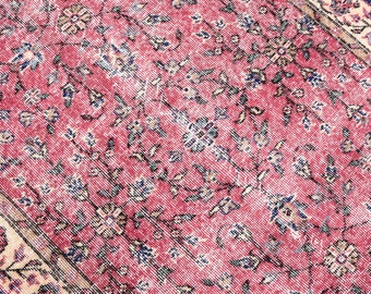 May include: A vintage rug with a pink and cream floral pattern. The rug has a faded, distressed look, giving it a unique and antique feel.