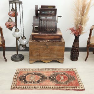 May include: A vintage-style rug with a geometric pattern in shades of red, brown, and beige. The rug is rectangular and placed on a light-colored floor. The scene includes antique furniture and decorative lamps.
