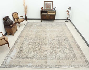 May include: A large, rectangular beige rug with an intricate, faded pattern dominates the room. The rug features a central medallion design and a border. The room also includes antique furniture and decorative items.