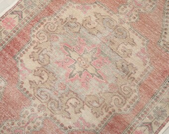 May include: A distressed rectangular rug with a central medallion design. The rug features a faded colour palette of pink, beige, and muted red. The pattern includes floral and geometric elements, creating a vintage aesthetic.