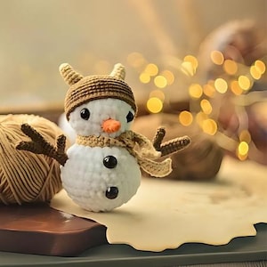 May include: A white crocheted snowman with brown yarn antlers, a brown crocheted hat, and a brown yarn scarf. The snowman is sitting on a brown surface with a blurry background of lights.
