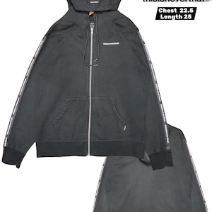 May include: Black zip-up hoodie with a hood and front pockets. The sleeves feature a white stripe with the text "thisisneverthat." The chest measures 22.5 inches, and the length is 25 inches. The brand logo "thisisneverthat" is visible.