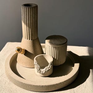 May include: A set of three concrete containers with a textured finish. The containers are in various shapes and sizes, and are arranged on a round, textured concrete tray.