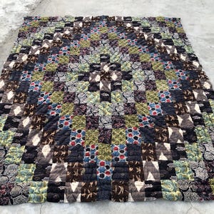 May include: A handmade quilt with a patchwork design. The quilt features a variety of patterned fabrics in shades of brown, blue, green, and gray. The quilt is rectangular and appears to be made of squares sewn together.
