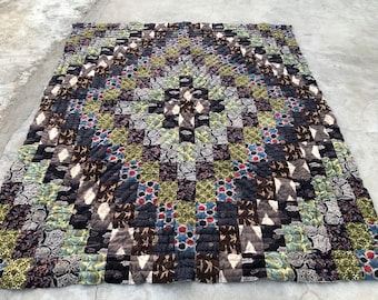 May include: A handmade quilt with a patchwork design. The quilt features a variety of patterned fabrics in shades of brown, blue, green, and gray. The quilt is rectangular and appears to be made of squares sewn together.