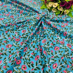 Puede incluir: Una vibrante tela turquesa con un estampado floral repetido. El diseño presenta flores rosas con hojas y tallos verdes. La tela está arrugada, creando pliegues y sombras.
