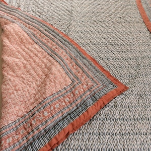 May include: A reversible quilt with a geometric pattern. One side features a peach-colored floral design, while the other side has a gray and white diamond pattern. The quilt is bordered with a striped design in peach, gray, and white.