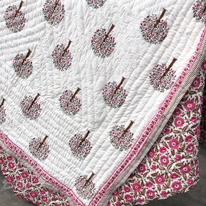 May include: White quilted blanket with a repeating pattern of stylized trees in shades of pink and brown. The border features a floral design in pink and brown. The blanket has a stitched, textured appearance.