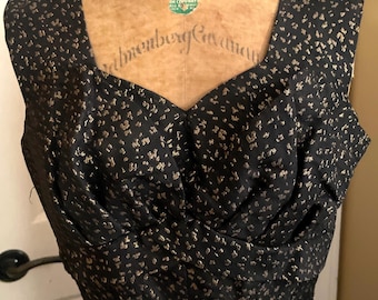 Può includere: Un abito nero vintage con scollatura quadrata e corpetto aderente. L'abito è adornato da un motivo maculato dorato. L'abito è esposto su un manichino vintage.