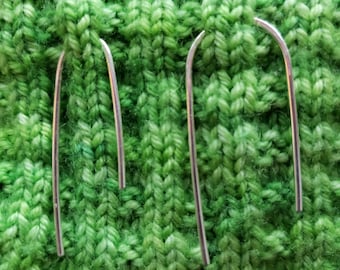 May include: Two silver-toned metal U-shaped earrings with a smooth, polished finish. The earrings feature a curved top and two parallel vertical bars, positioned against a textured, vibrant green knitted fabric background.