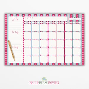 May include: A colorful monthly planner with a pink, blue, and white design. The planner includes sections for goals, to-do lists, and ideas, with a gold pen resting on the side. The calendar grid is divided into squares for each day of the month.
