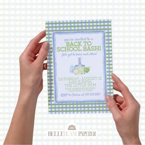 Può includere: Un invito rettangolare con un bordo a quadretti blu e verde, con il testo "BACK TO SCHOOL BASHI". L'invito include i dettagli dell'evento come data, ora e luogo, con un'illustrazione a tema scolastico. L'invito è tenuto da due mani.