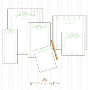 May include: A collection of stationery items, including notepads and a to-do list, in various sizes. The items feature a light green bow design and the name "chelsea" in a script font. A gold pen rests on the stationery. The Belle Blanc Papier logo is at the bottom.