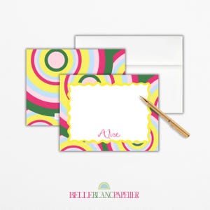 Puede incluir: Juego de papelería con un diseño retro colorido. El juego incluye una tarjeta de notas con un borde amarillo festoneado, el nombre "Alice" en escritura rosa y un sobre a juego. Un bolígrafo dorado descansa sobre la tarjeta. El fondo presenta un patrón repetido de rayas coloridas.