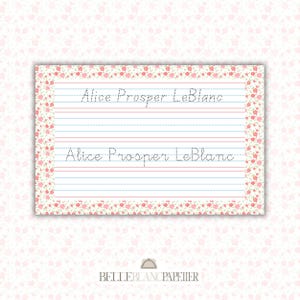 May include: A stationery sheet with the name "Alice Prosper LeBlanc" written in cursive. The sheet has blue and red lines for writing practice. The border is decorated with a floral pattern in pink and green. The BelleBlancPapetier logo is at the bottom.