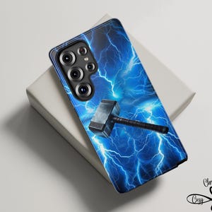 May include: A phone case featuring a blue lightning storm design with a silver and black hammer. The case has a black camera module and is resting on a white surface. The design includes the text "Christina's Cozy Cache".