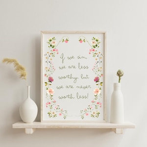 May include: A framed print with the text "If we sin, we are less worthy, but we are never worth less!" surrounded by a floral wreath. The print is displayed on a white shelf with a vase and a bottle.